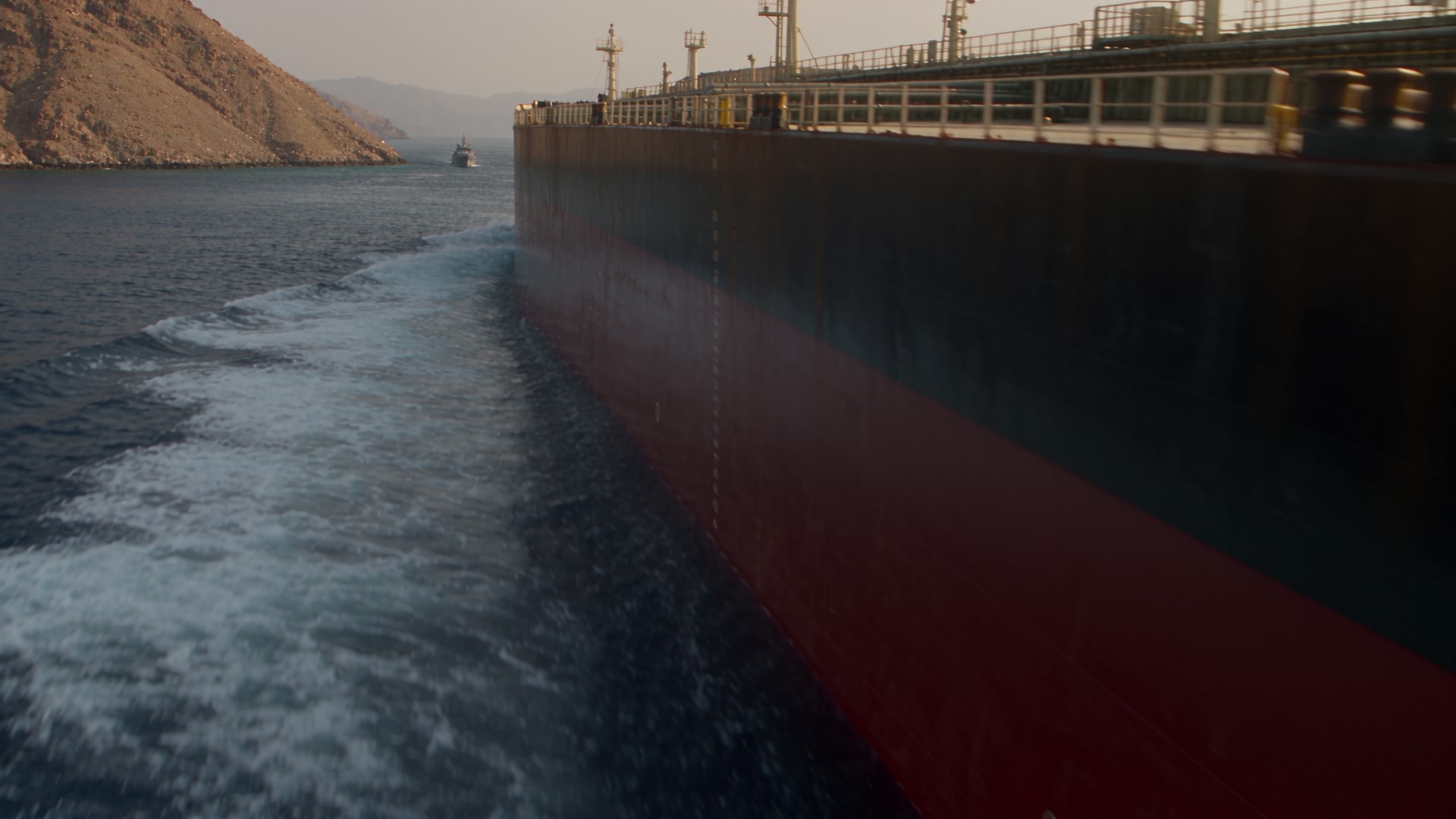 A crude-oil tanker passes through dark water beside a mountainous coastline.